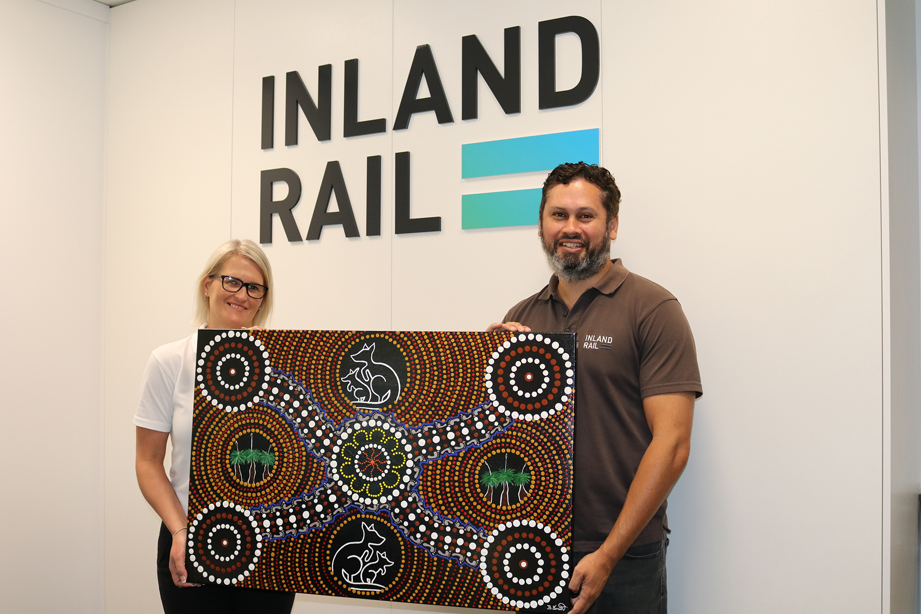 Inland Rail staff standing in Toowoomba office reception holding a piece of Indigenous artwork by Western Wakka Wakka artist, Belinda Smith
