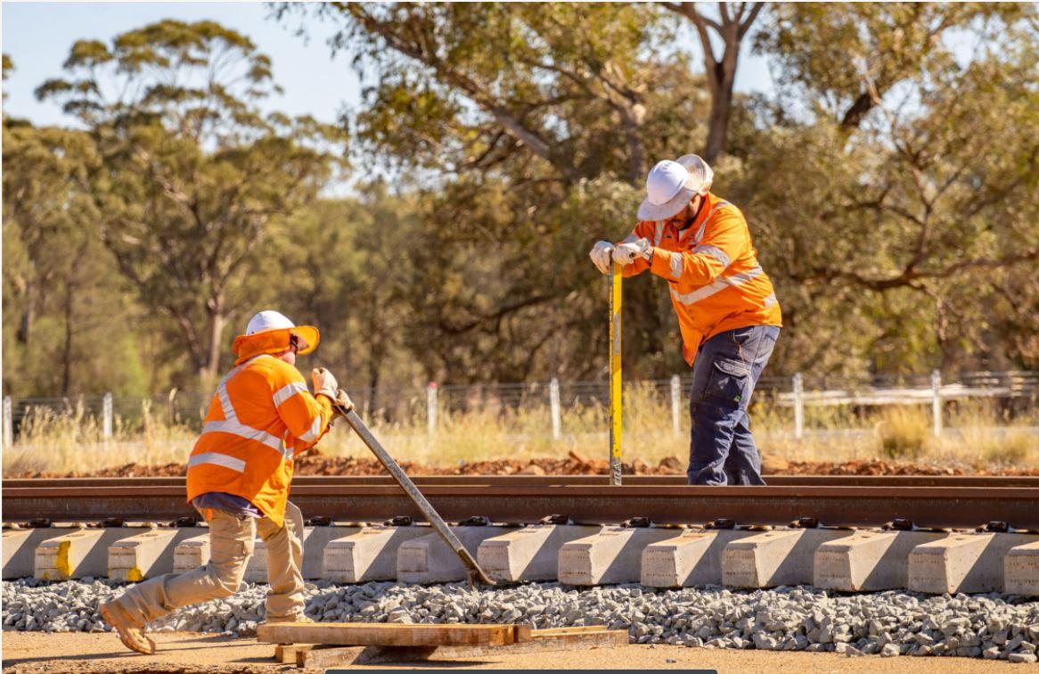 Two workers on the rail line helping to install track