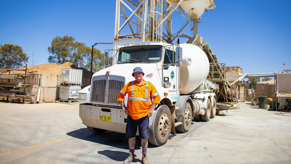 Image of a man dressed in PPE standing in front of a cement truck
