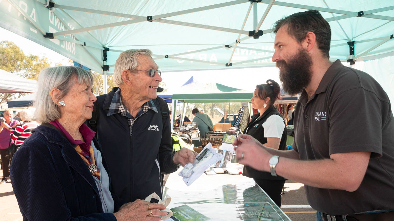 Image of an Inland Rail employee talking to two elderly community members at a market drop-in session.