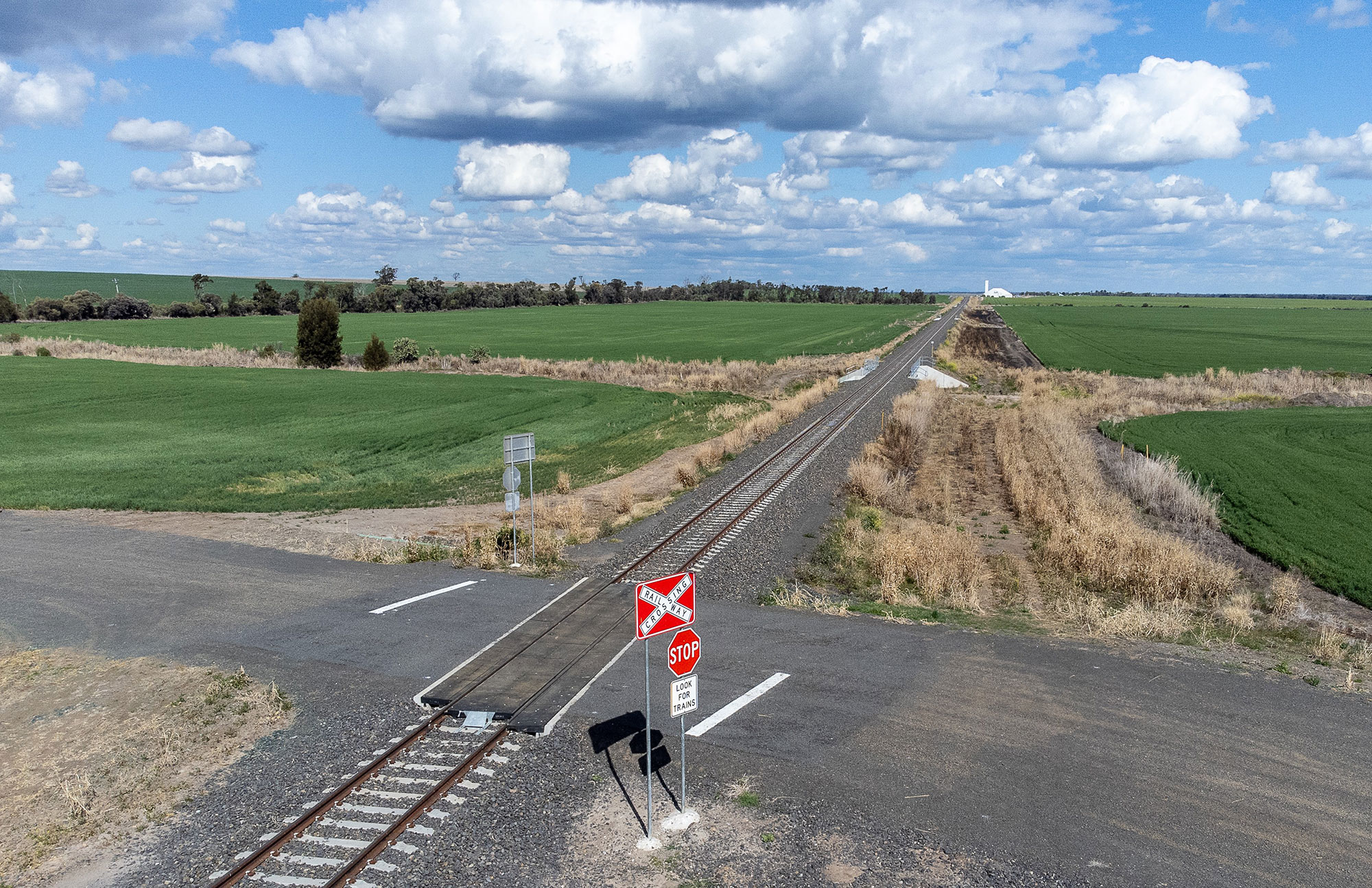 An upgraded private level crossing with bigger and brighter signage and new rubber crossing panels, in Crooble with GrainCorp silos in the background